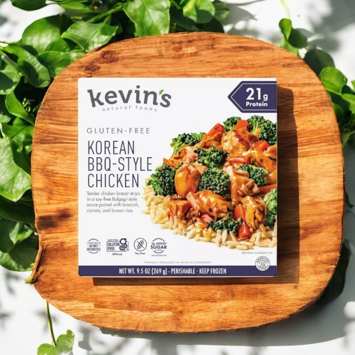 A 9.5 oz package of Kevin's 4 Pack Combo rests on wood, surrounded by green leaves. The box emphasizes gluten-free gourmet meals with 21g protein and displays an image of the chef-crafted dish.
