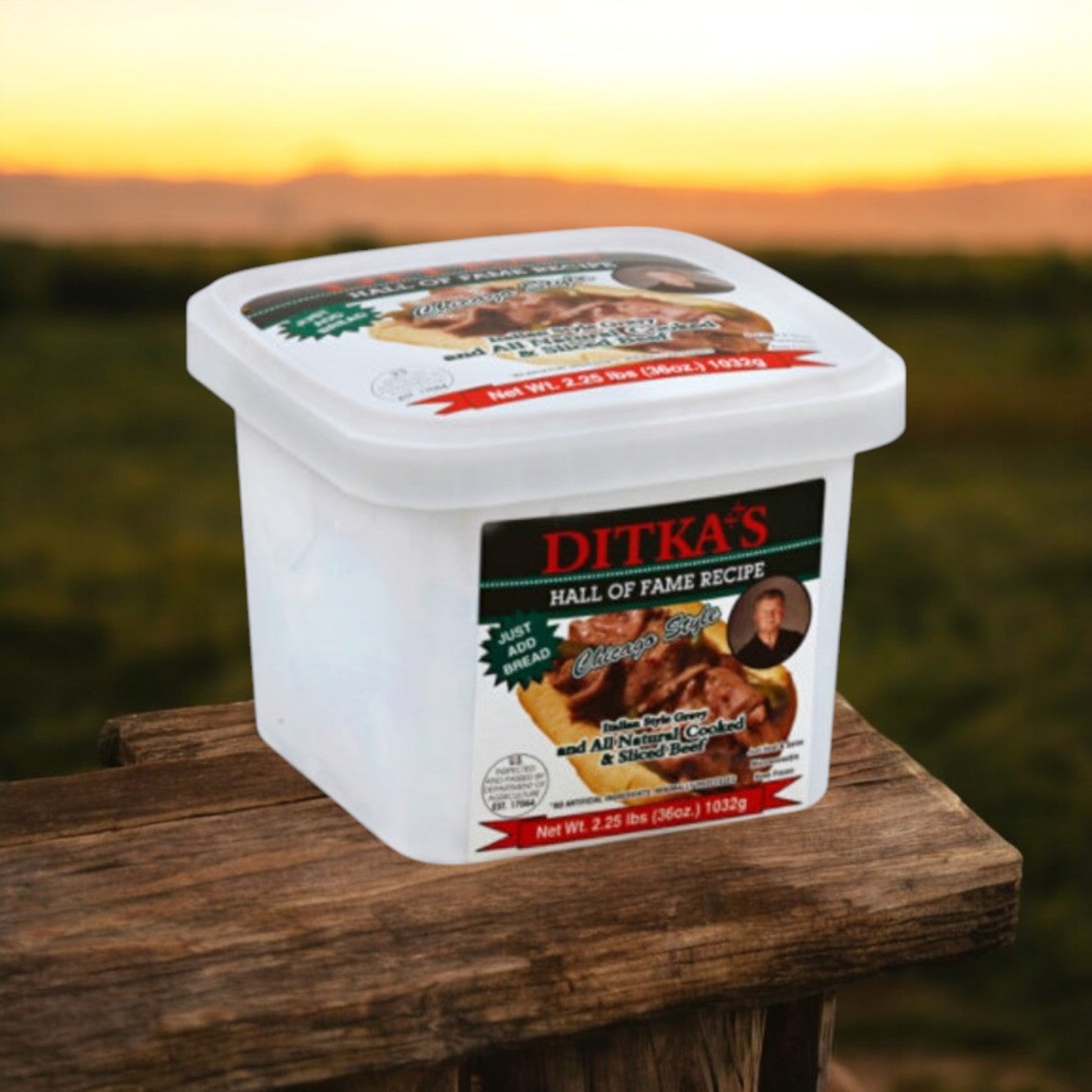 A container of Ditka's Italian Beef, Chicago Style (2.25 lb.), from Vienna Beef, rests on a wooden table against a blurred outdoor sunset background, capturing the essence of Chicago cuisine.