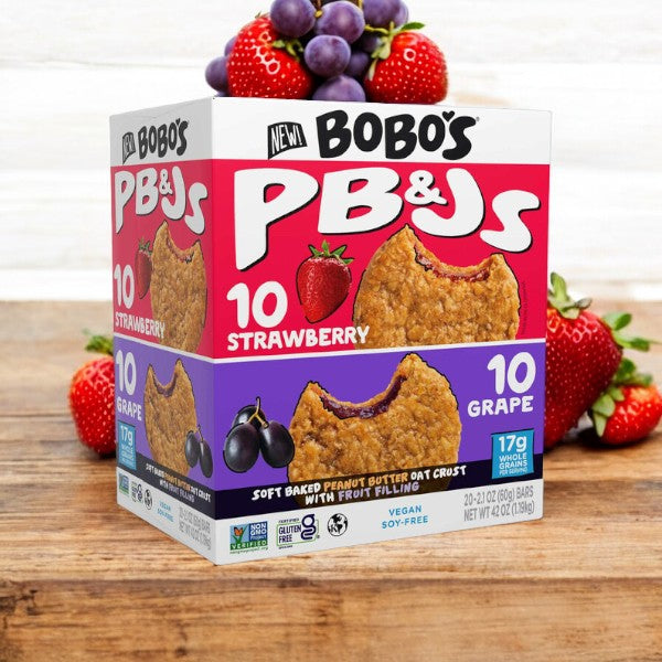 A 20-count variety pack of Easy Lunches Bobo's PB&Js Oat Sandwich Bar, featuring an assortment of strawberry and grape flavors with 10 bars of each. The packaging showcases 17g of whole grains per bar along with vegan and soy-free attributes, set against a backdrop of fresh strawberries and grapes.