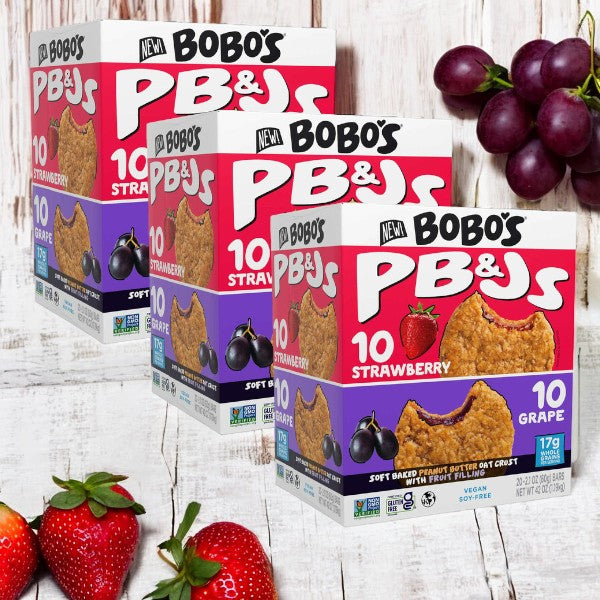 Displays of Easy Lunches' Bobo's PB&Js Oat Sandwich Bar variety pack (20-count per box, 60 total sandwiches) in strawberry and grape flavors are showcased. Each box features product images and nutritional information, set against a background featuring strawberries, grapes, and a wooden surface.