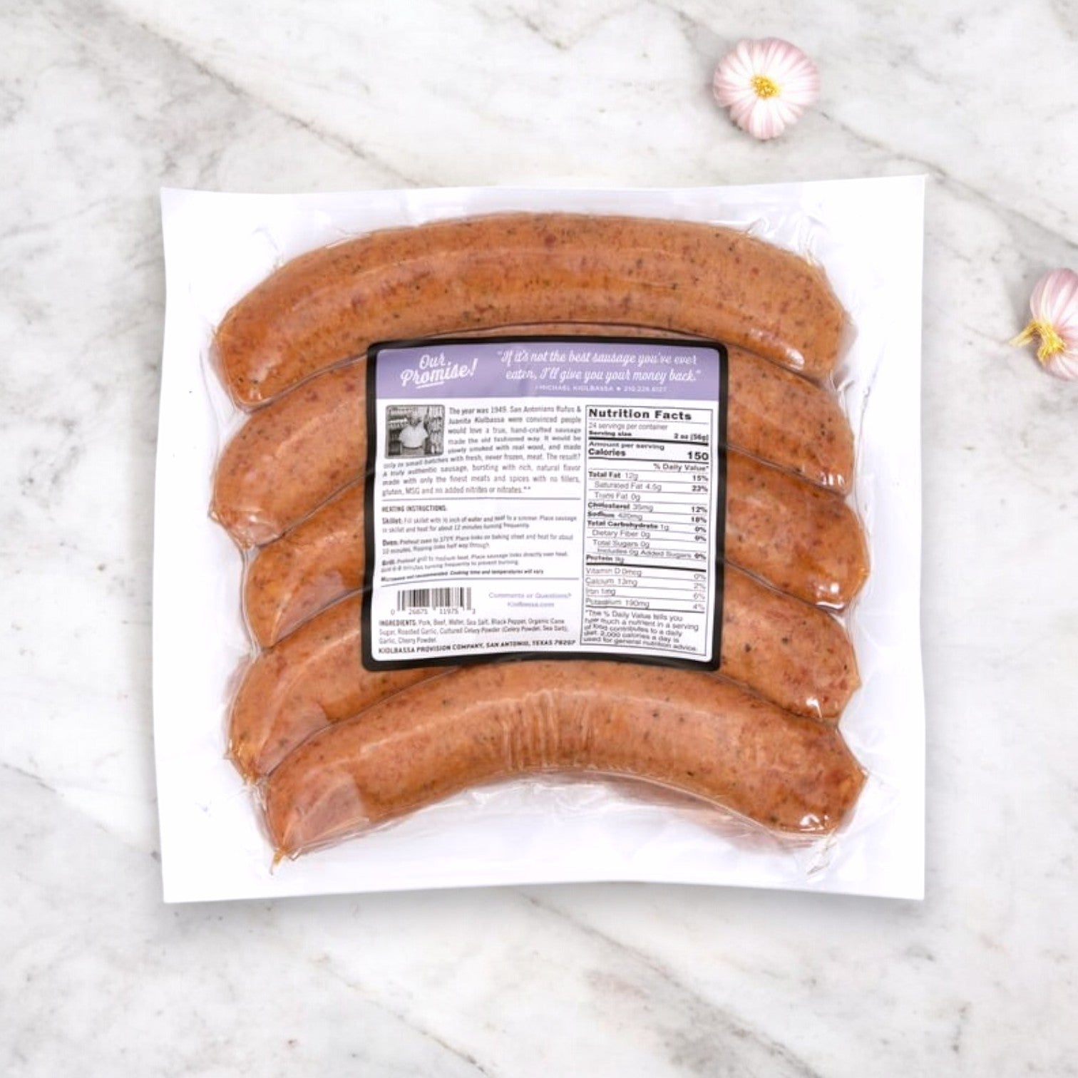 A vacuum-sealed pack of Kiolbassa Roasted Garlic Smoked Sausages, crafted from premium-quality pork and offering a bold, smoky flavor, is artfully presented on a marble surface with flowers. The label features nutrition facts and a quote from the manufacturer.