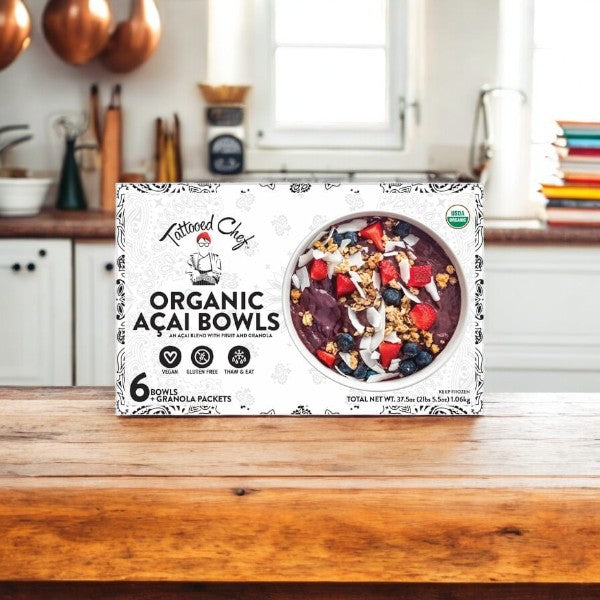 A box of Tattooed Chef Organic Acai Bowls, 6-count, vegan and gluten-free, rests on a wooden kitchen counter with a white kitchen in the background.