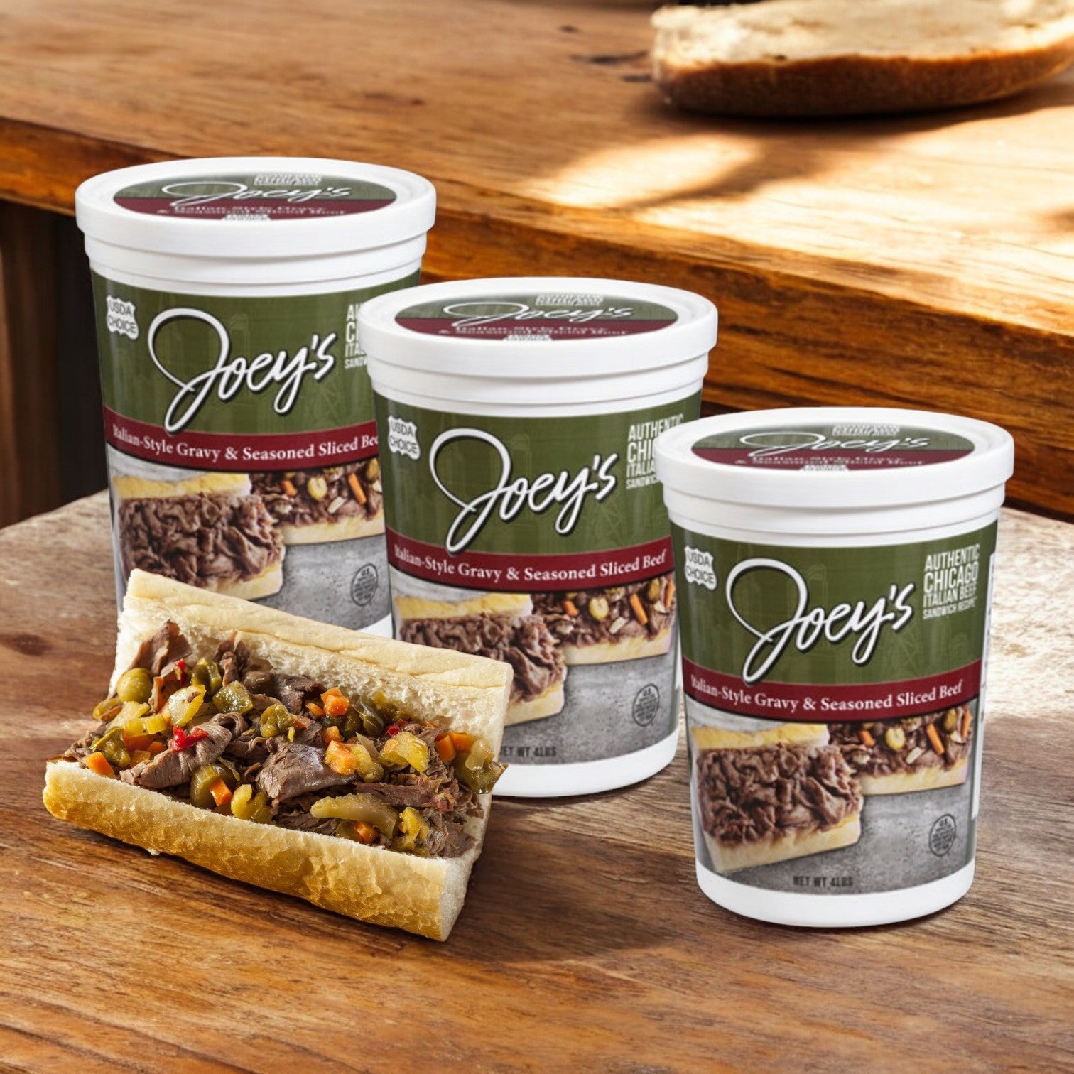 Three Easy Lunches Joey’s Sliced Beef, Gravy & Seasoned, Italian-Style containers are displayed on a wooden surface next to a sandwich filled with the savory beef and toppings.