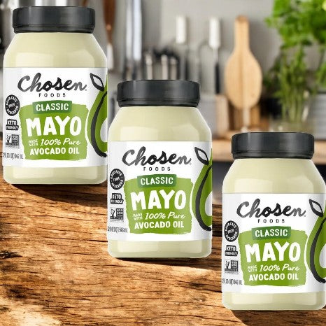 Three jars of Chosen Foods Avocado Oil Classic Mayo, 32 fl oz each, rest on a wooden surface against a cozy kitchen backdrop. This gluten-free mayo offers a healthier alternative to traditional options, ideal for those prioritizing taste and wellness.