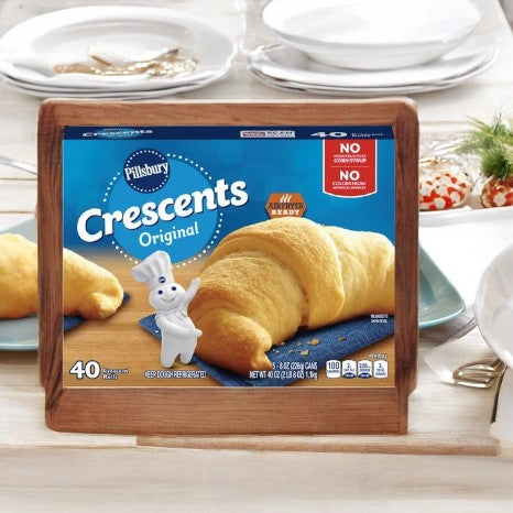 A box of Pillsbury Crescents- 1 Count by Pillsbury, featuring pre-made dough for effortless baking, is elegantly displayed on a wooden stand with plates and a beautifully decorated table in the background.