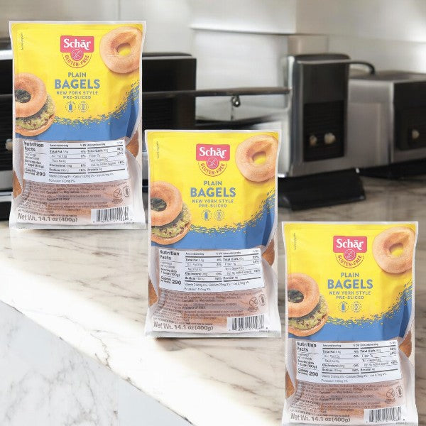 Three packages of Schar's Gluten-Free New York Style Plain Bagels, pre-sliced for convenience, sit on a marble kitchen counter—ideal for those with gluten sensitivities craving authentic bagel flavors.