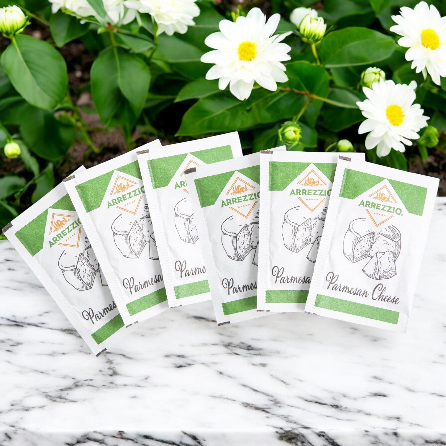 Packets of parmesan cheese sit on a marble surface with white flowers and green leaves, ideal for enhancing your Buona Marinara Sauce & Meatballs Kit + Italian Beef - 12 Total Sandwiches!!.