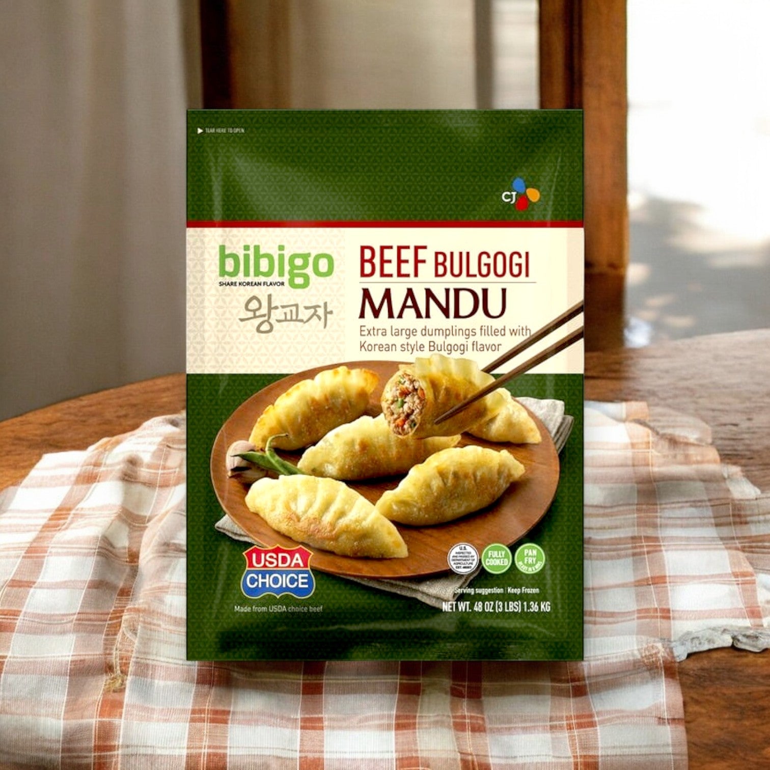 A 3-lb package of CJ Bibigo Beef Bulgogi Mandu Dumplings sits on a striped cloth, featuring images of Korean-style dumplings and a USDA Choice logo, promising an authentic taste adventure.