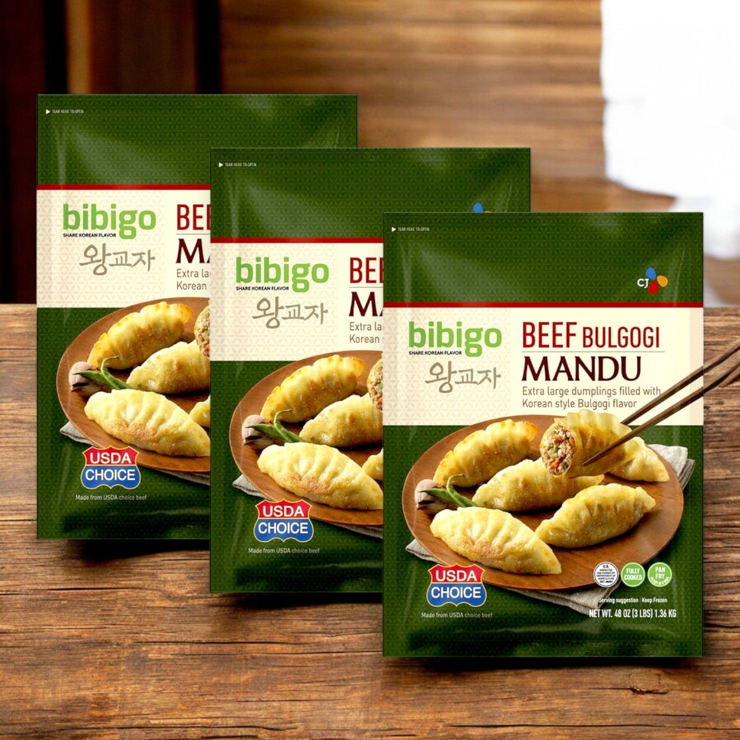 Three packages of CJ Bibigo Beef Bulgogi Mandu Dumplings are prominently displayed on a wooden surface, embodying authentic Korean flavor. Each pack features tempting dumpling images and proudly displays the USDA Choice label.