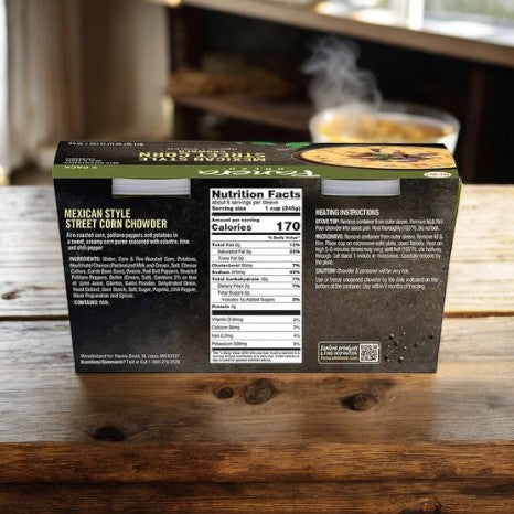 A box of Panera Mexican Style Street Corn Chowder, 24 oz, from Panera Bread is on a wooden table with nutrition facts and heating instructions visible. In the background, a bowl of steaming soup highlights elote and roasted poblano peppers for an authentic touch.