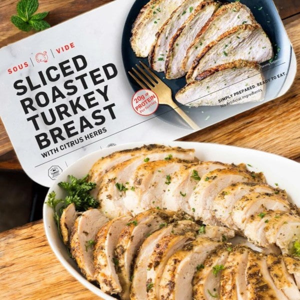 Cuisine Solutions' Sliced Turkey Breast with Citrus Herbs-1 Count, known for its high protein and masterful sous vide preparation, sits next to freshly cut slices on a wooden table.