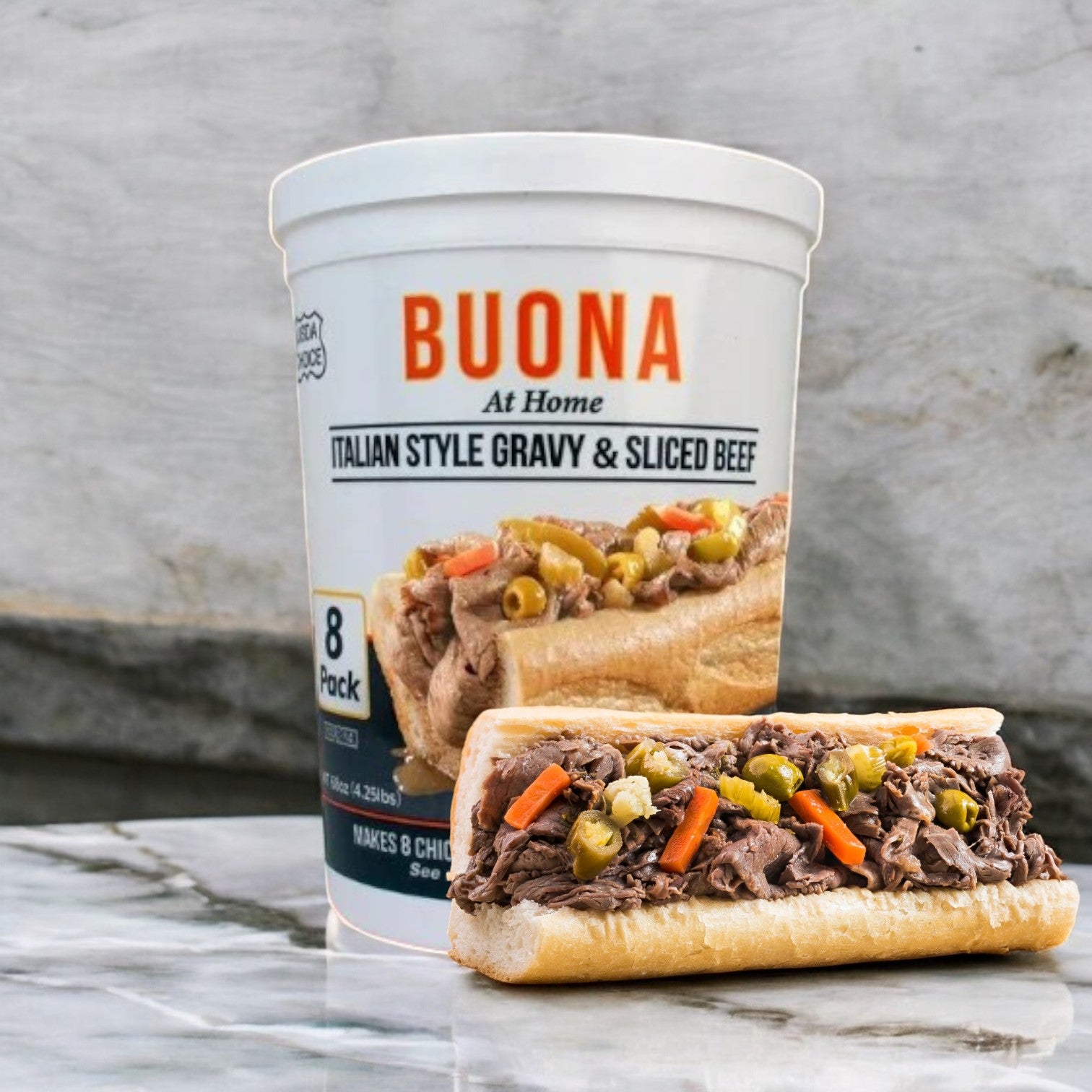 A container of Buona Gravy & Sliced Beef, Italian Style, from the 8 pack-1 Count, is shown with a Chicago classic sandwich of Italian beef and vegetables on a marble surface.