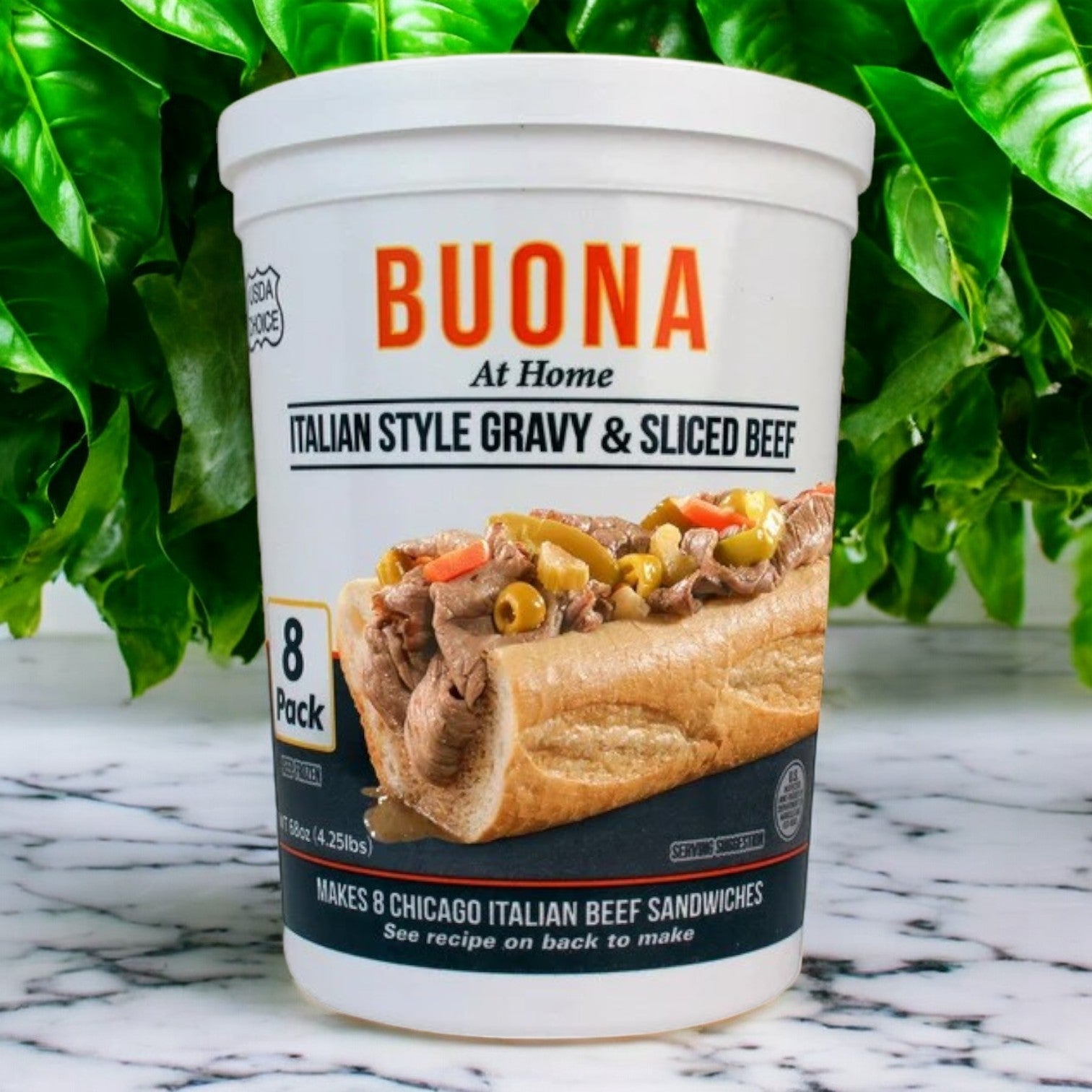 The container labeled "Buona Italian Style Gravy and Sliced Beef, 68 oz,-1ct," features an Italian beef sandwich with peppers, paying homage to classic Chicago street food. It includes enough packs to make eight sandwiches. Green leaves in the background suggest the freshness of a cherished family recipe.