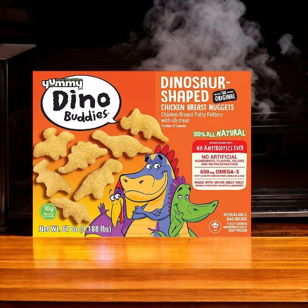 A box of Yummy Dino Buddies Chicken Nuggets from Easy Lunches, weighing 67 ounces per case, sits next to an open toaster oven. These dinosaur-shaped treats feature all-natural ingredients and are free from antibiotics, highlighting the high-quality products offered by Member's Mark at competitive prices.