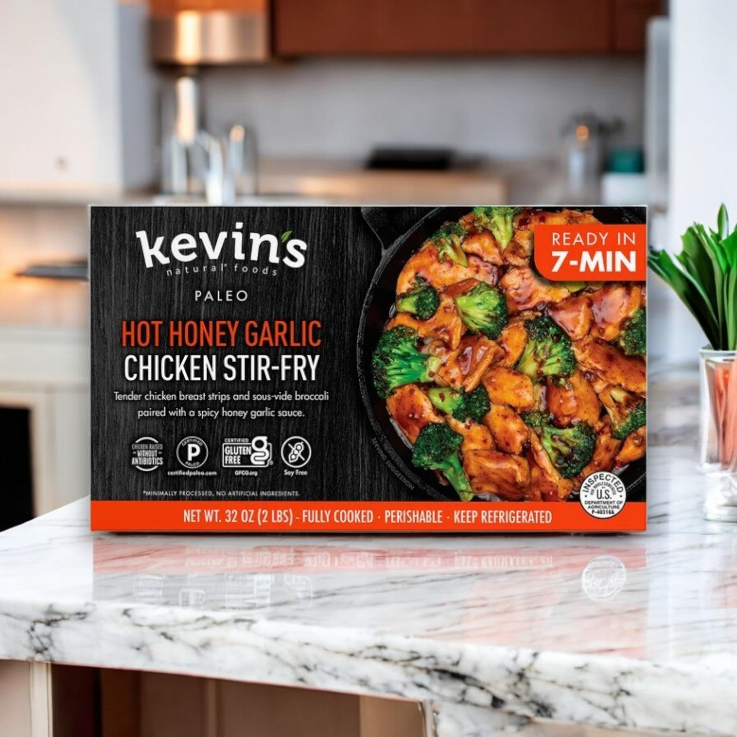 A 32 oz box of Kevin's Natural Foods Hot Honey Chicken Stir Fry features a tempting dish with broccoli on a countertop, made using antibiotic-free chicken and offering a gluten-free treat for everyone.