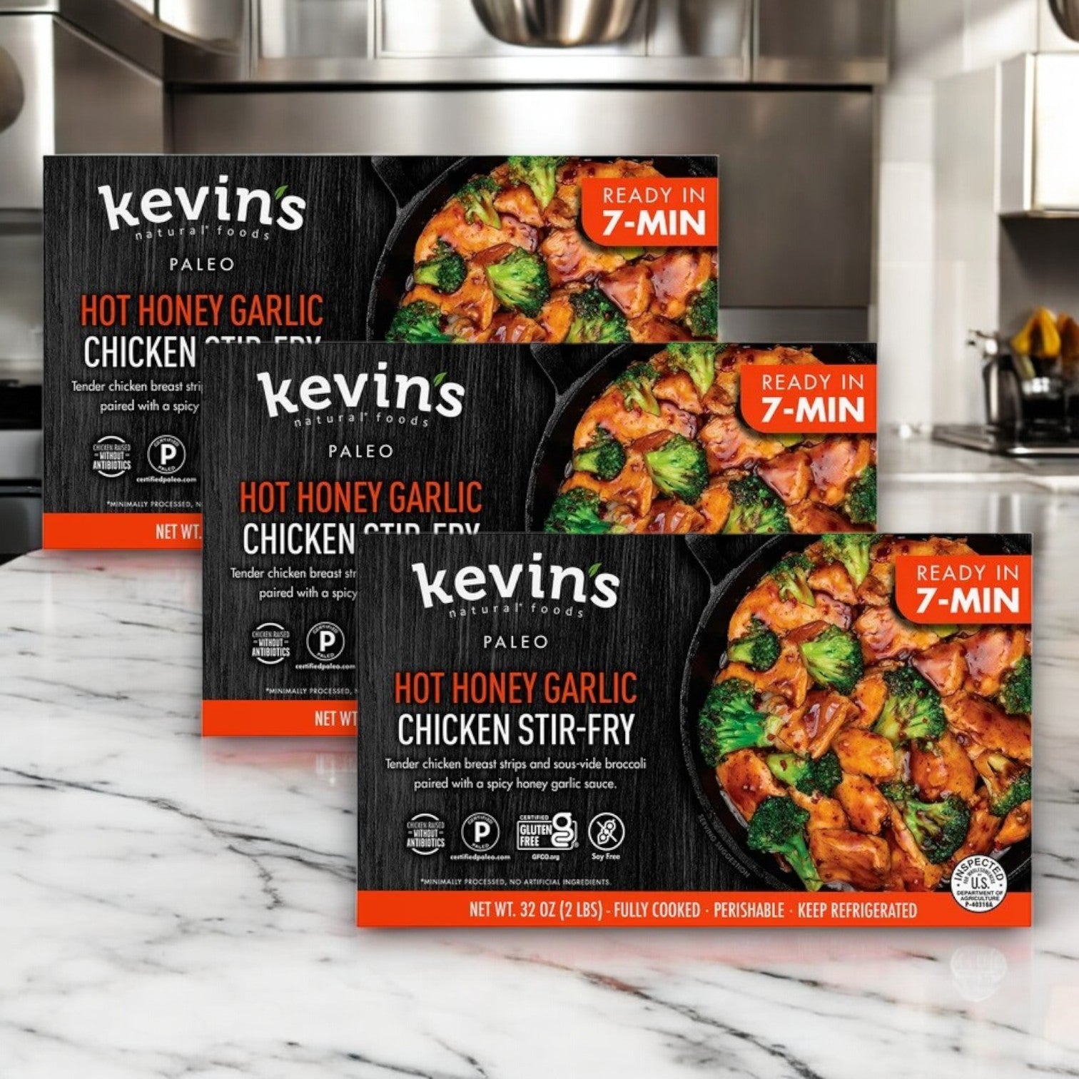 Displayed are three boxes of Kevin's Natural Foods Hot Honey Chicken Stir Fry, 32 oz. - 3 Count. The packaging highlights that it's made with antibiotic-free chicken, paleo, fully cooked, gluten-free, and ready in just 7 minutes.