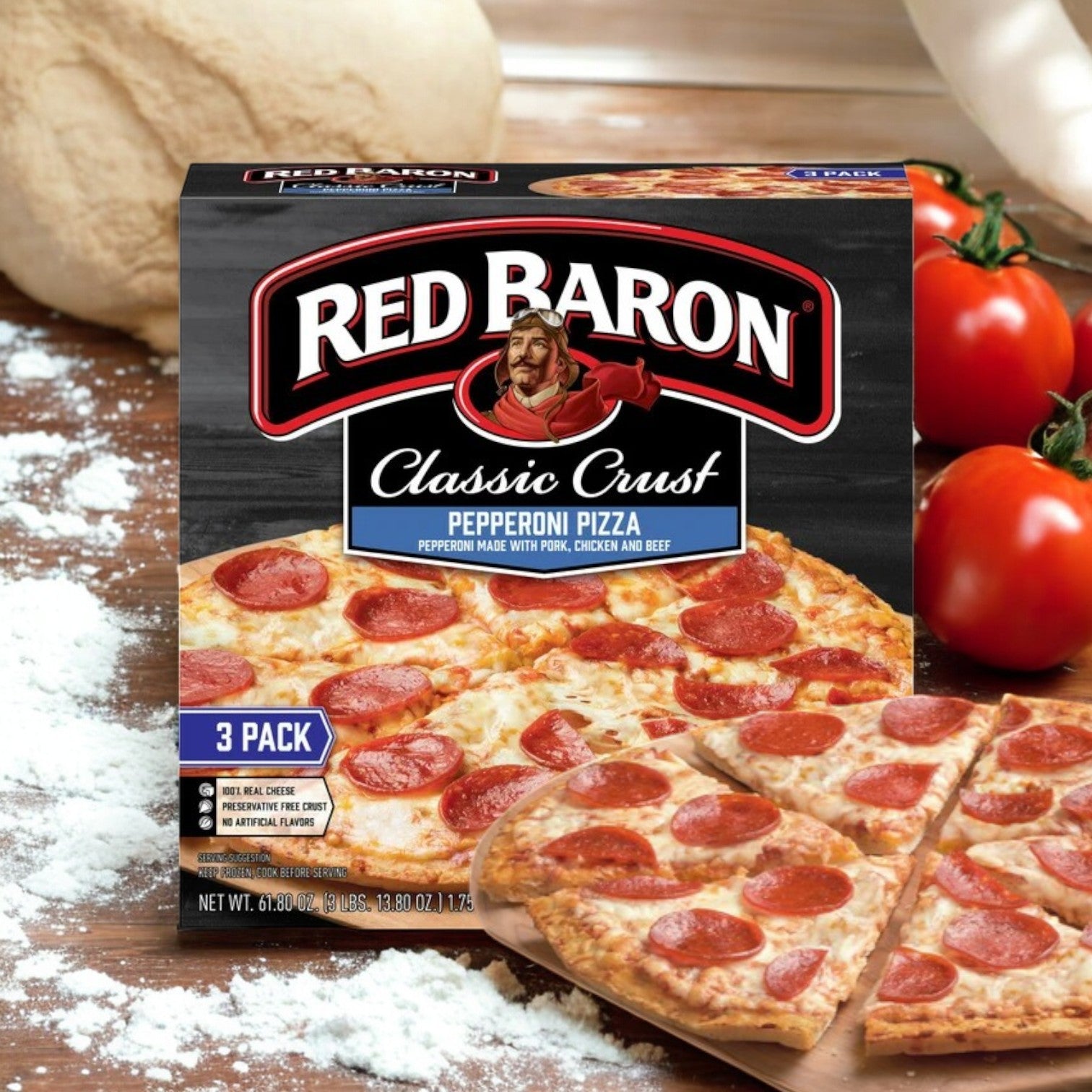 A box of Red Baron Pepperoni Classic Crust Frozen Pizza is beautifully presented on a rustic wooden surface, surrounded by scattered flour and ripe tomatoes, with a tempting slice prominently displayed in front.