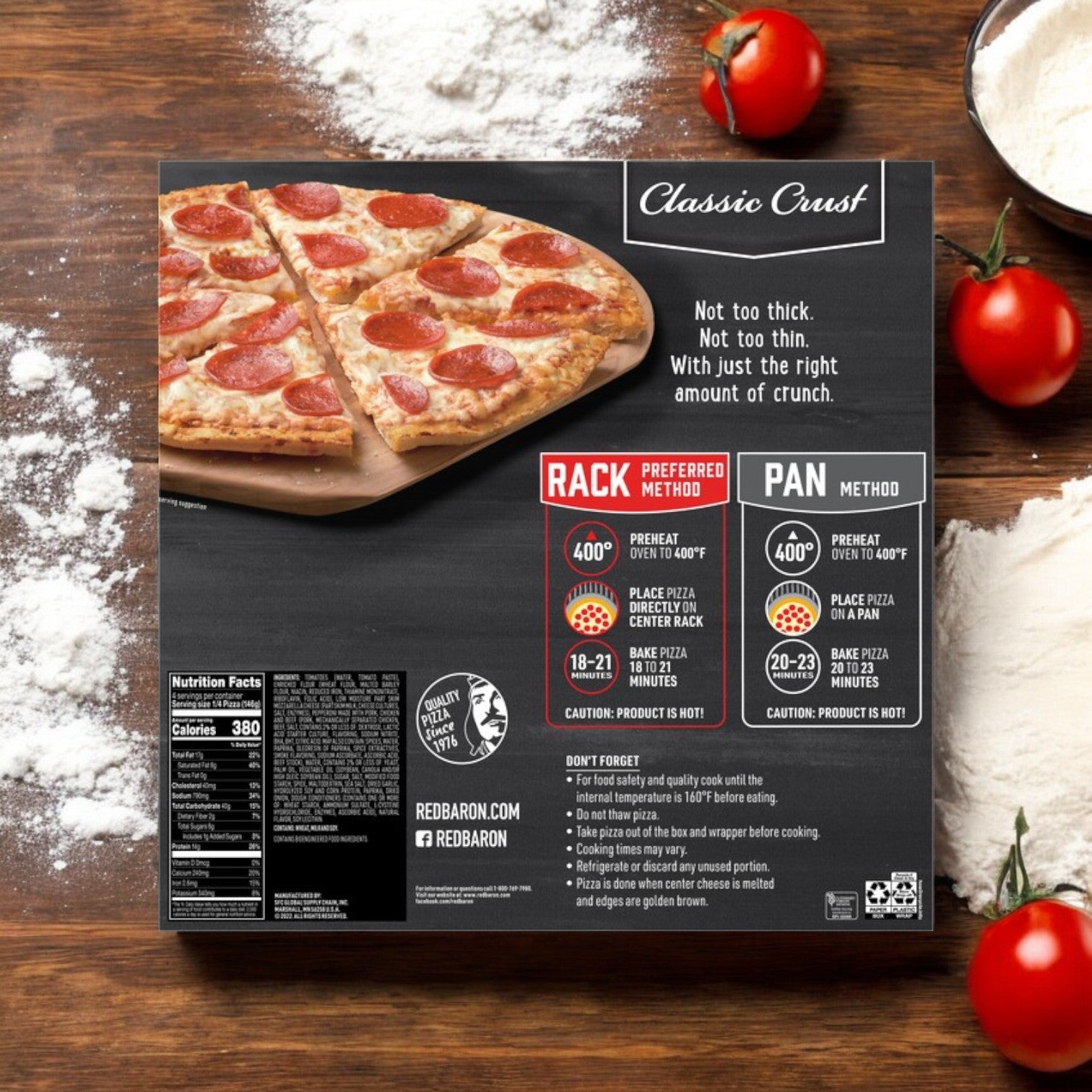 The Red Baron Pepperoni Classic Crust Frozen Pizza box rests on a flour-dusted wooden surface, surrounded by ripe tomatoes. It includes baking instructions and nutritional information.