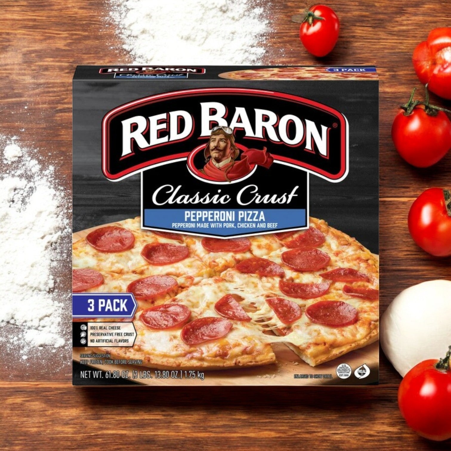 On a wooden surface, a Red Baron Pepperoni Classic Crust Frozen Pizza sits in its box, surrounded by scattered flour, ripe tomatoes, and an onion—exemplifying classic crust perfection.