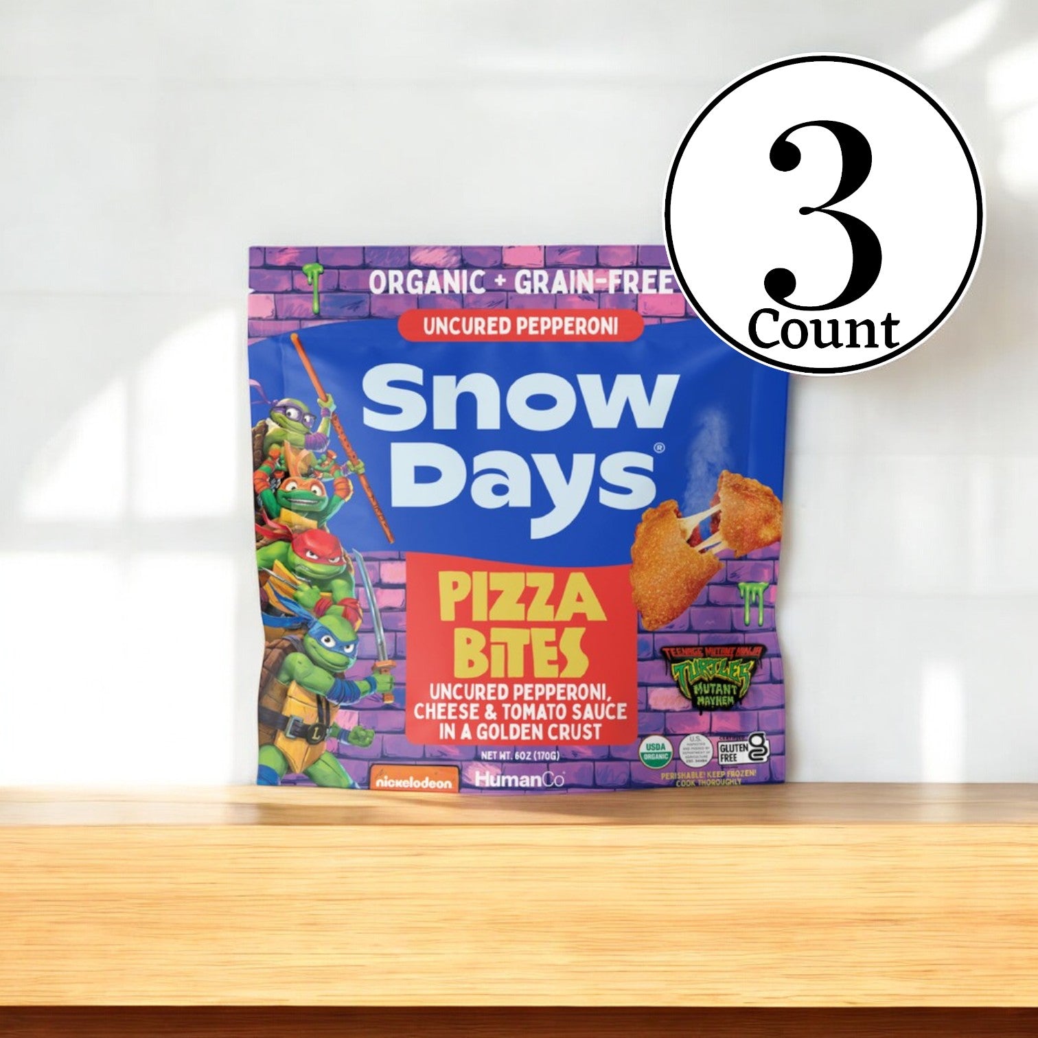 A package of Snow Days Uncured Pepperoni Pizza Bites, which is organic, gluten-free, and grain-free with cartoon characters on the bag. Each pack contains 6 oz., and the product comes in a "3 Count" label. Ideal for those looking for a high-protein snack!