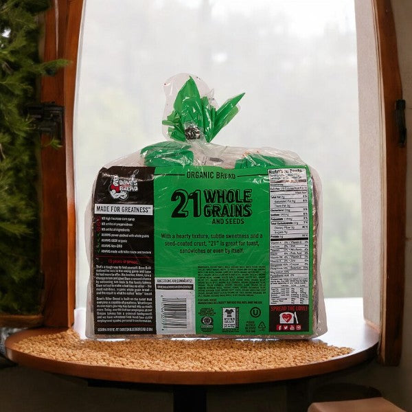 A bag of Dave's Killer Bread Organic 21 Whole Grain - 1 Count is placed on a round table in front of a window. The product's nutritional information and branding, including its USDA Organic and Non-GMO certifications, are visible on the back of the package.