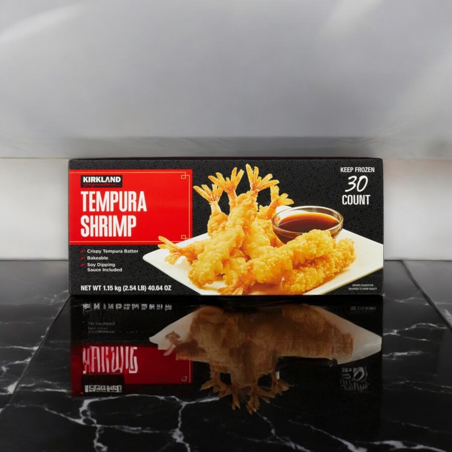 A box of Kirkland Signature Tempura Shrimp, 2.35 lbs, 30-count - 1 Pack, rests on a black marble surface, featuring an image of golden shrimp enveloped in crispy tempura batter accompanied by a small bowl of dipping sauce. Ideal for those desiring quick preparation without compromising taste.