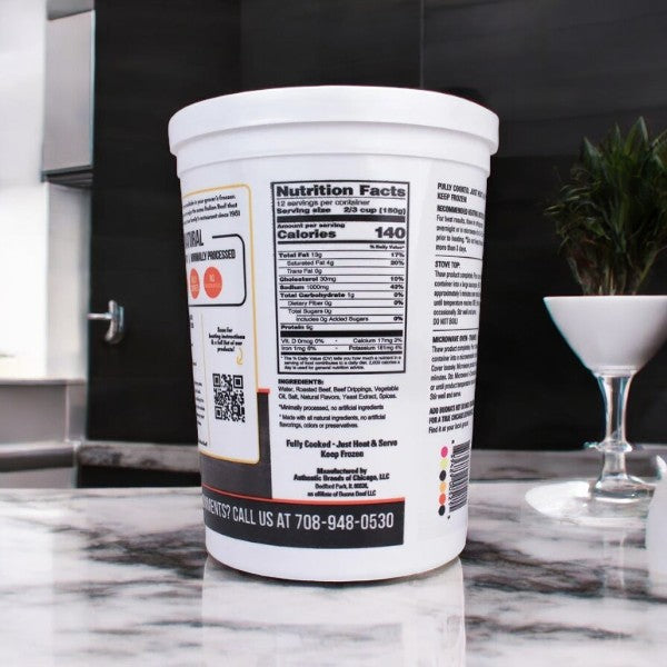 A Buona Gravy & Sliced Beef container sits on a marble countertop revealing its nutrition facts, while a nearby stemmed glass with greenery adds elegance, evoking the savory warmth of a Chicago classic Italian beef feast.