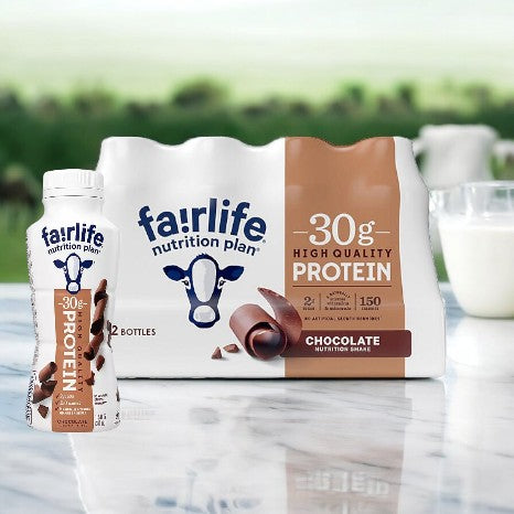 The FairLife Nutrition Plan 30g Protein Shake, Chocolate-18 Pack, stands prominently against a blurred countryside backdrop, making it an ideal choice for post-workout recovery with its high-protein formula offering 30g per shake.