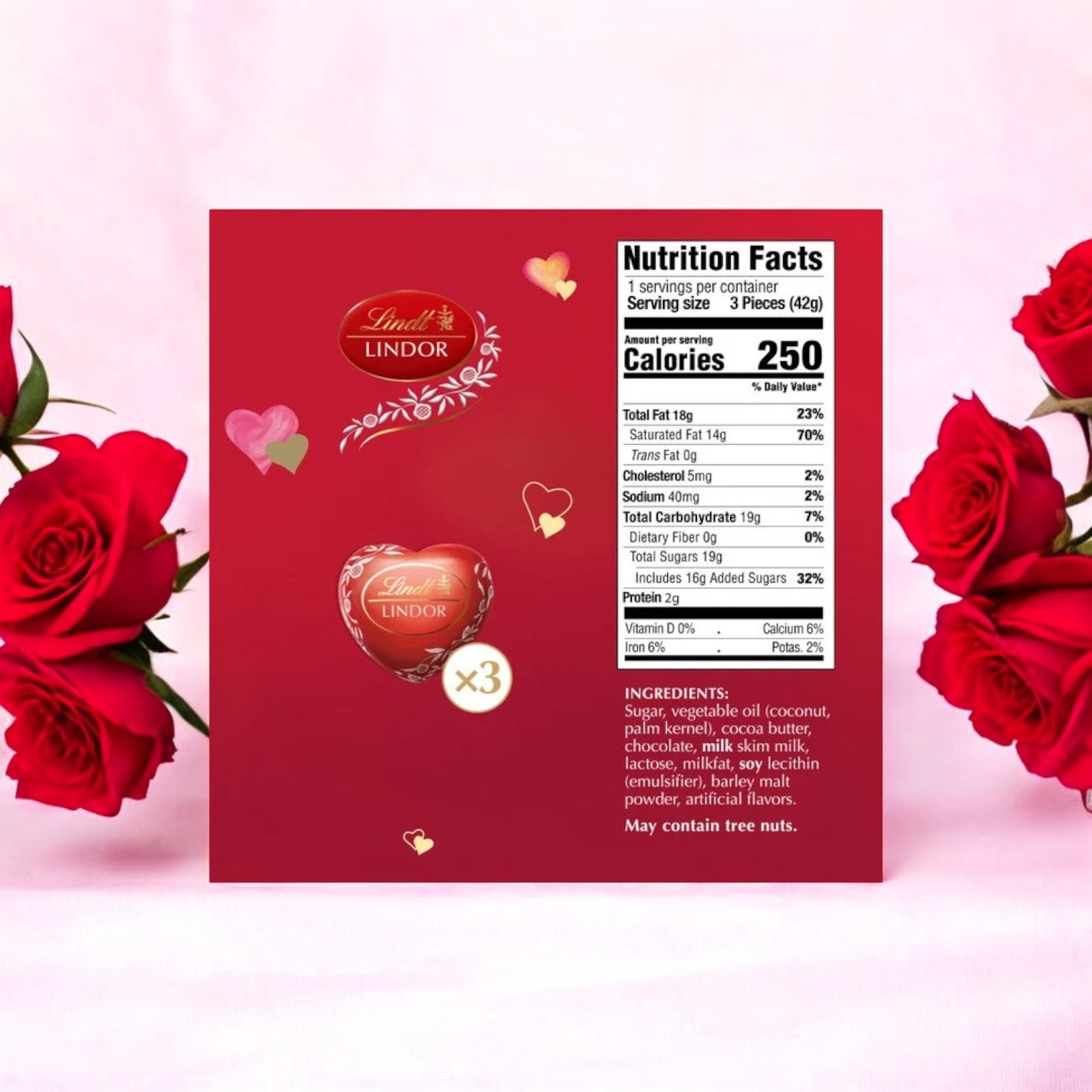 The Lindt Lindor Valentine's Milk Chocolate Candy Truffles Heart Gift Box, 1.5 oz-3 count, features red packaging with nutrition facts and ingredients, surrounded by red roses on a soft pink background, making it the perfect Valentine's gift.