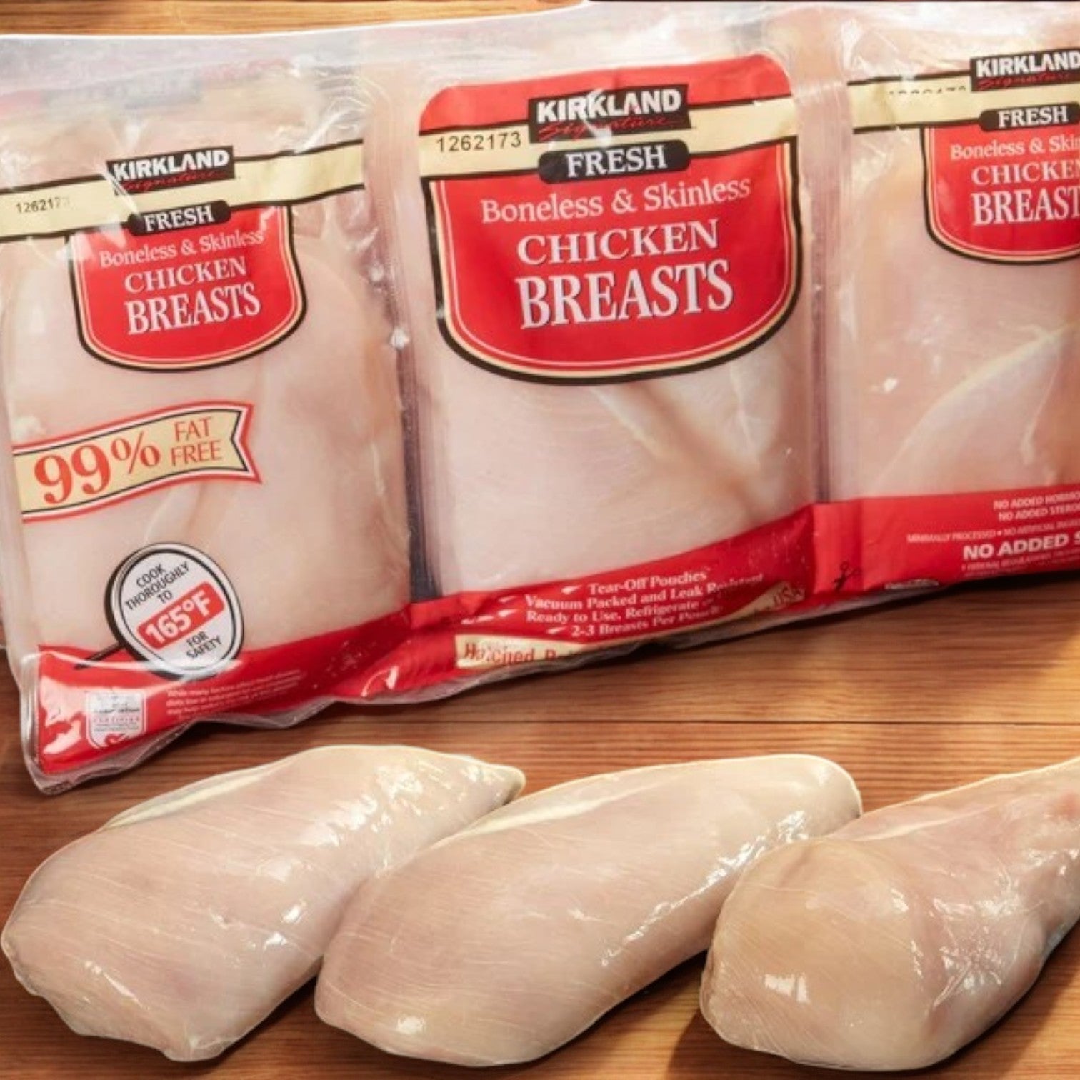 Kirkland Signature "Air Chilled" Fresh Boneless Skinless Chicken Breast packages rest on a wooden surface with three uncooked chicken breasts in front.