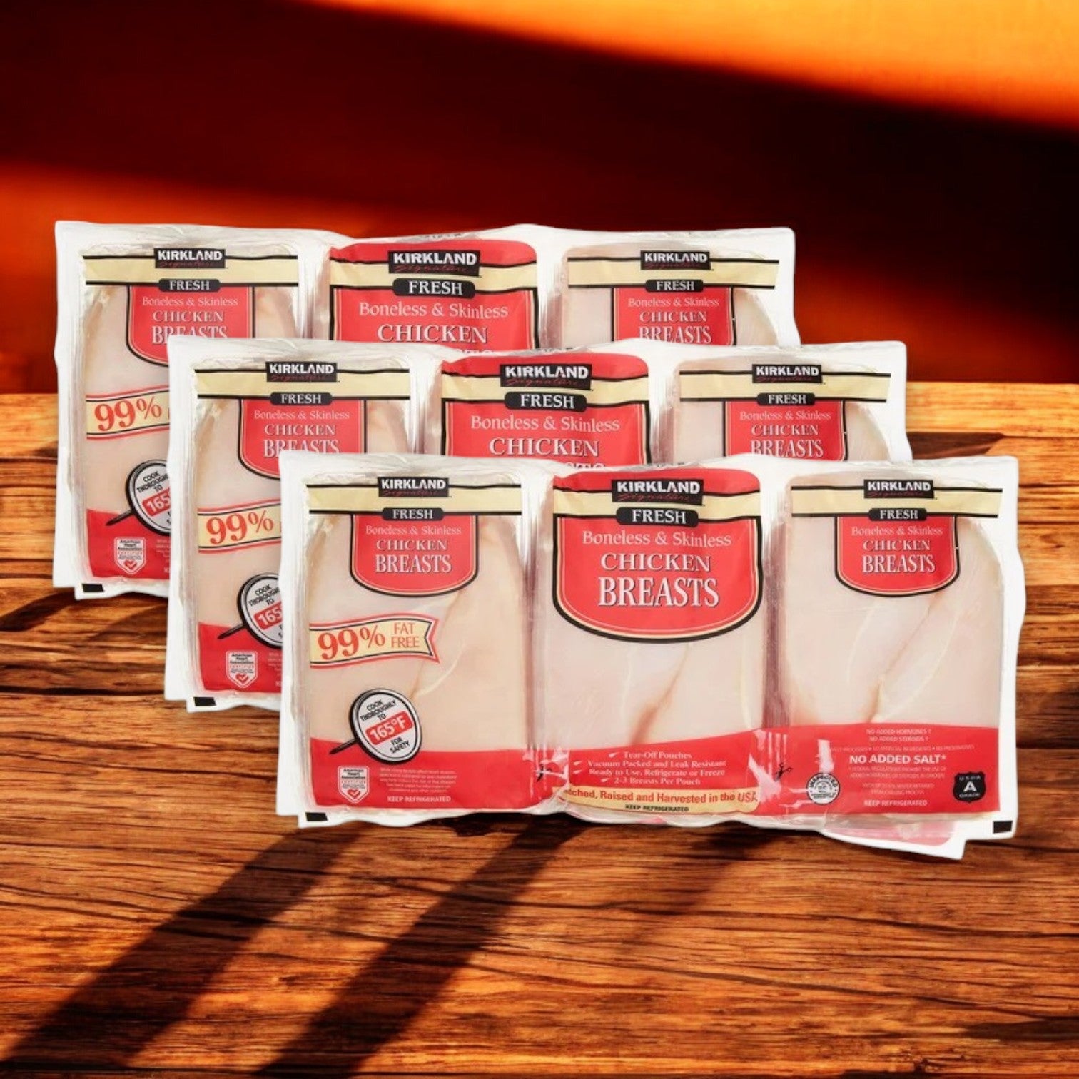 Kirkland Signature "Air Chilled" Fresh Boneless Skinless Chicken Breast in packs of three, featuring USDA Grade A and 99% fat-free quality, are arranged in two rows on a wooden surface.