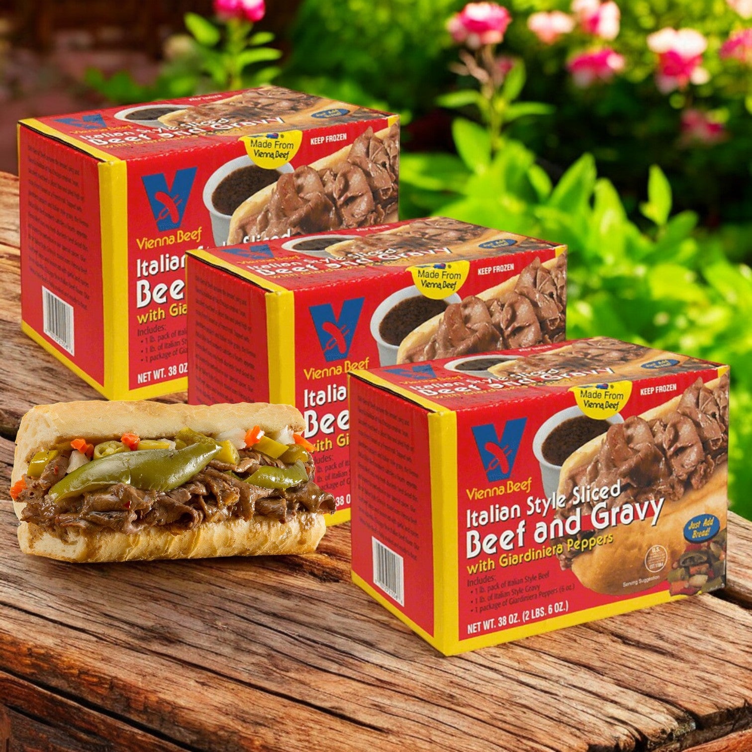 On a wooden table, there are three boxes of Vienna Beef Italian Style Sliced Beef and Gravy with Giardiniera Peppers. In front, a sandwich is filled with Italian beef, gravy, and peppers.