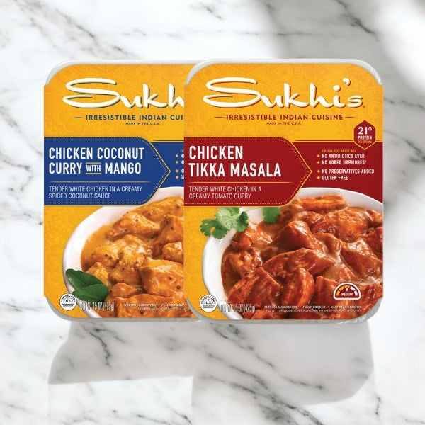 Two packaged Indian cuisine meals, "Tikka Masala Family Entree Meal" and "Chicken Coconut Curry with Mango," from the Easy Lunches brand, are displayed on a marble surface. These 15 oz ready-to-eat meals feature vibrant images of the respective dishes.