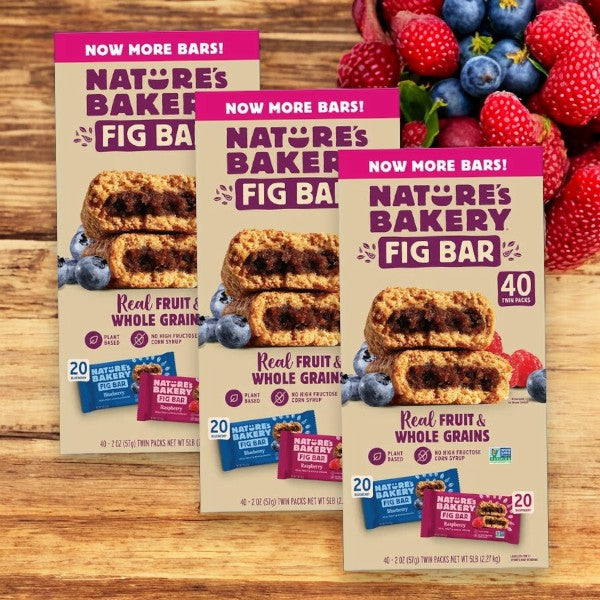 Three cases of Easy Lunches' Nature's Bakery Fig Bar Variety Pack are displayed with a variety of berries in the background. The packaging highlights that the fig bars are made with real fruit and whole grains, and each case contains 40 twin packs.