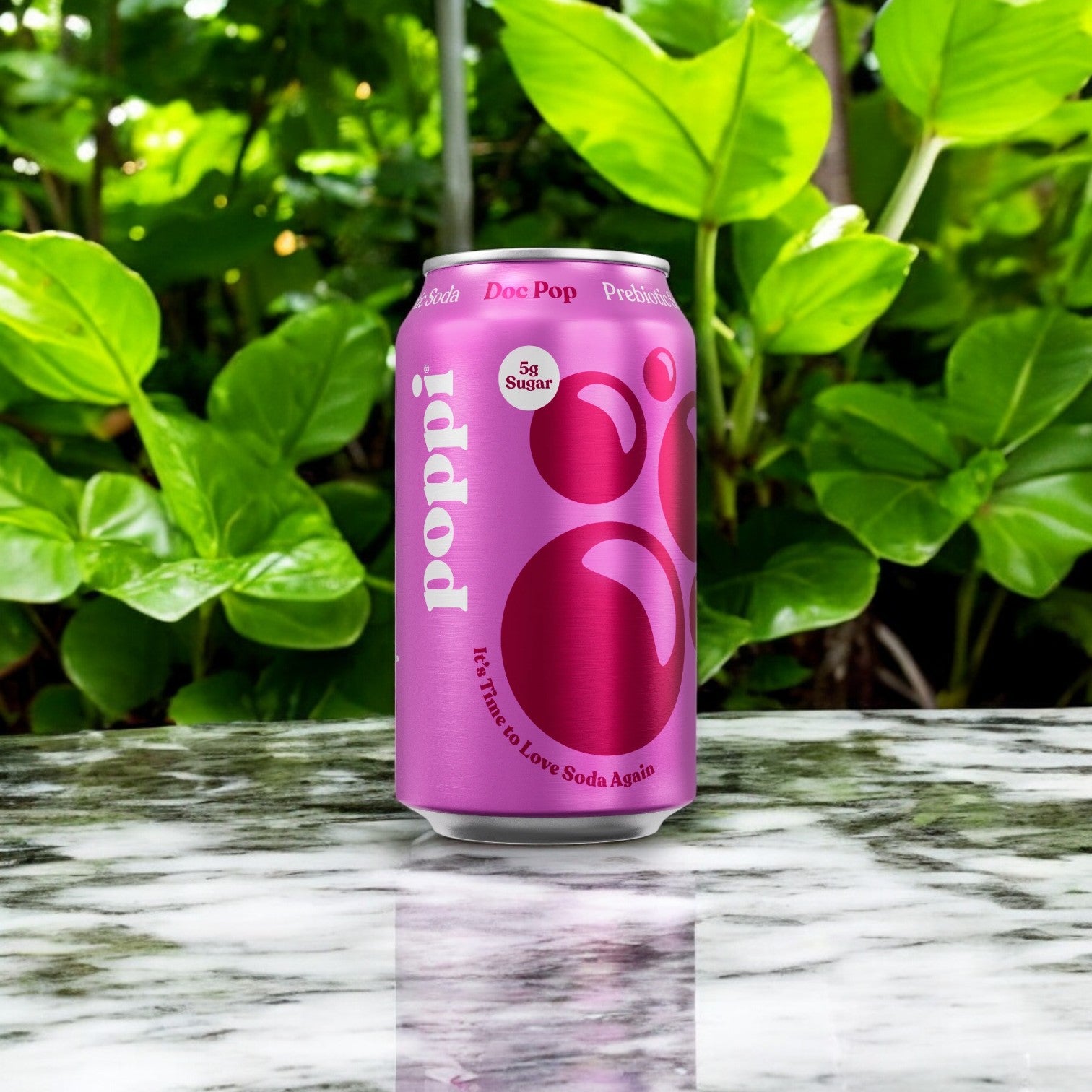 A can of Poppi Prebiotic Soda, Doc Pop flavor from a 4-pack (12 fl oz each), sits on a marble surface, surrounded by green leaves.