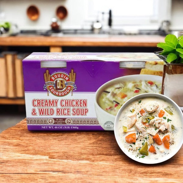 A Boulder Organic Boudin Creamy Chicken & Wild Rice Soup, 24 oz, 2-count-1 Pack sits on a wooden counter. Its steaming bowl offers creamy comfort in every spoonful against the cozy kitchen backdrop.