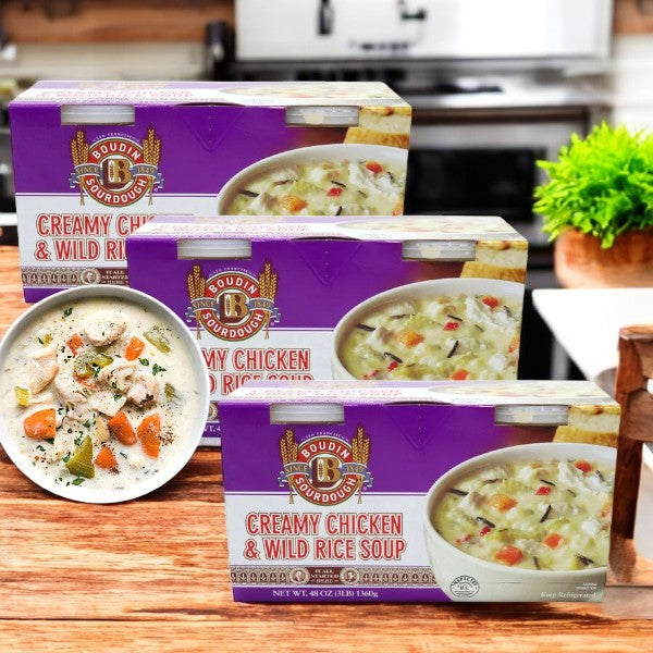 Two boxes of Boulder Organic Boudin Creamy Chicken & Wild Rice Soup, 24 oz, 2-count-3 packs, are on the kitchen counter, with a bowl of the creamy soup in the foreground.