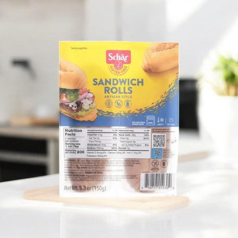 A Schär Sandwich Rolls package, Gluten-Free and Artisan Style-1 Count, rests on the counter with the Schar brand logo and nutritional info. The front boasts an enticing Artisan Style image of rolls, highlighting quality and flavor.