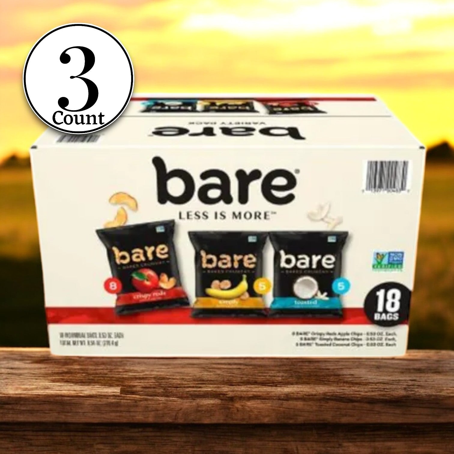 A box labeled "Bare Snacks: Less is more" is placed on a wooden surface, containing 18 bags of Bare Baked Crunchy Variety Pack Chips. These healthy snacks come in apple, banana, and coconut flavors. Text on the packaging reads "3 Boxes Total." In the background, there's an inviting outdoor scene perfect for enjoying fruit chips.