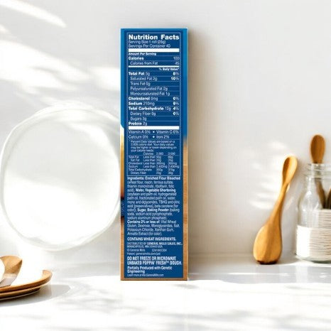 A cereal box nutrition label is displayed. Nearby, wooden utensils, a glass jar, and a can of Pillsbury Crescents rest on a white surface with bright lighting.