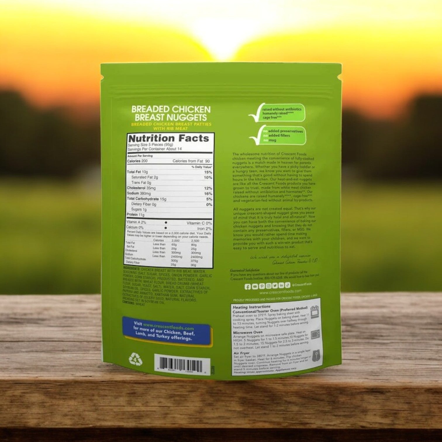 The backside of a green Crescent Foods package showcases Halal All Natural Chicken Breast Nuggets with nutrition facts and instructions on a wooden table, set against a blurred sunset background, making them an ideal, natural choice for your dining delight.