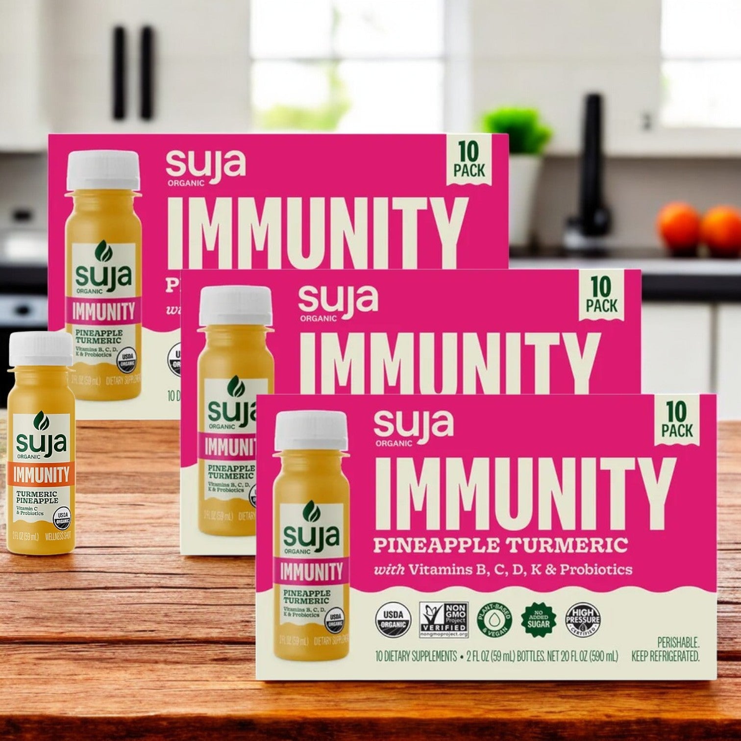 Three packs of Suja Organic Immunity Defense Shots, each containing 10 bottles, sit on the kitchen counter. They feature organic ingredients with vitamins B, C, D, K and a potent probiotic strain for optimal health benefits.