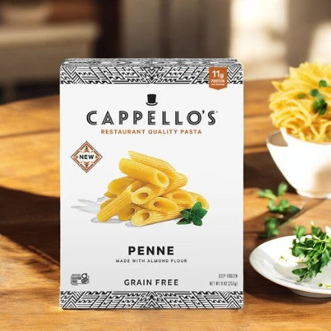 A box of Cappello's Penne Pasta- 1 Count from the brand Cappello's, made with almond flour and gluten-free, is displayed on a wooden table next to a small plant and a bowl of herbs.