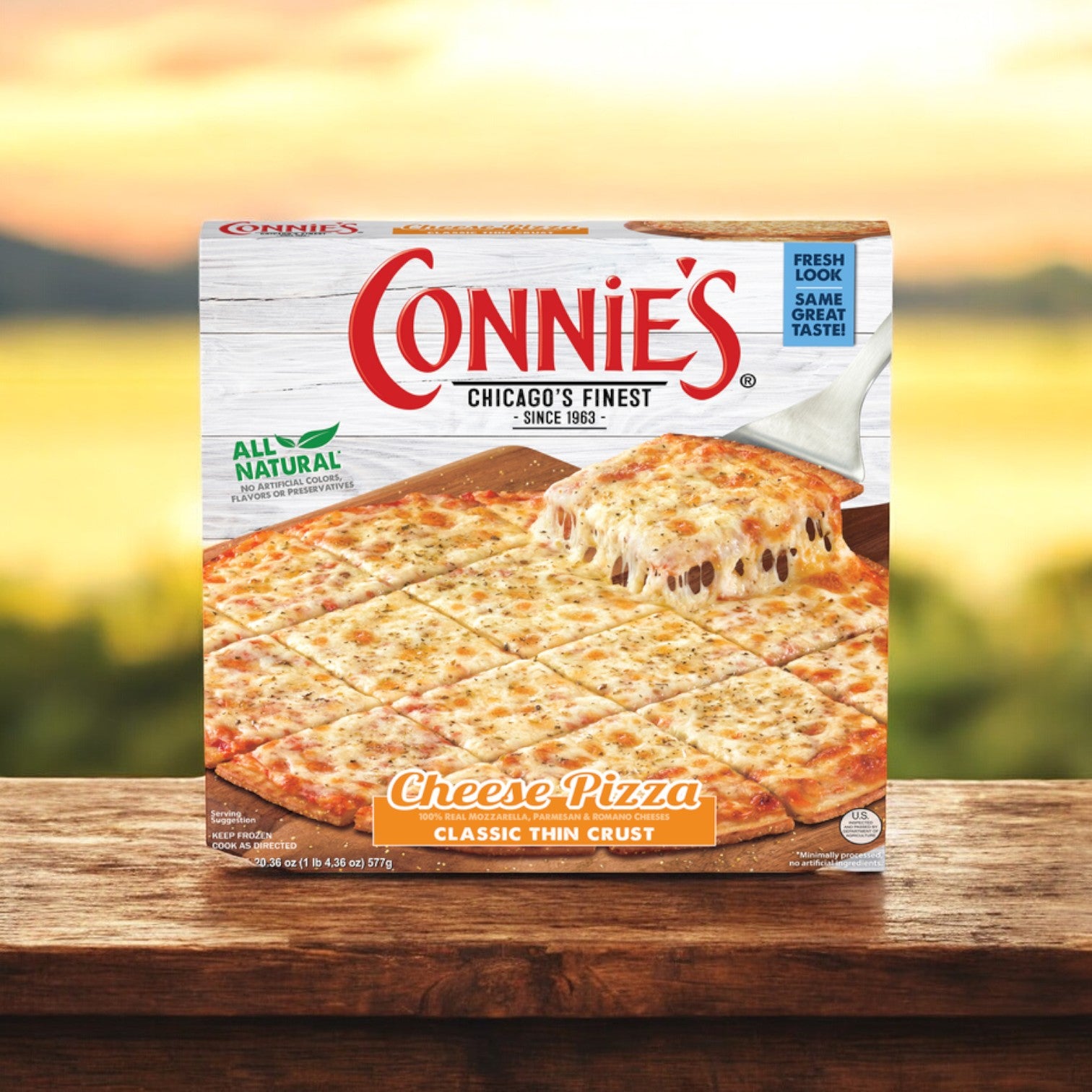 The Connie's Pizza Classic Thin Crust Cheese Pizza, a 20.36 oz single pack, is elegantly displayed on a wooden table. In the background, slices of pizza with a crispy thin crust and a rich cheese blend promise to delight your taste buds.