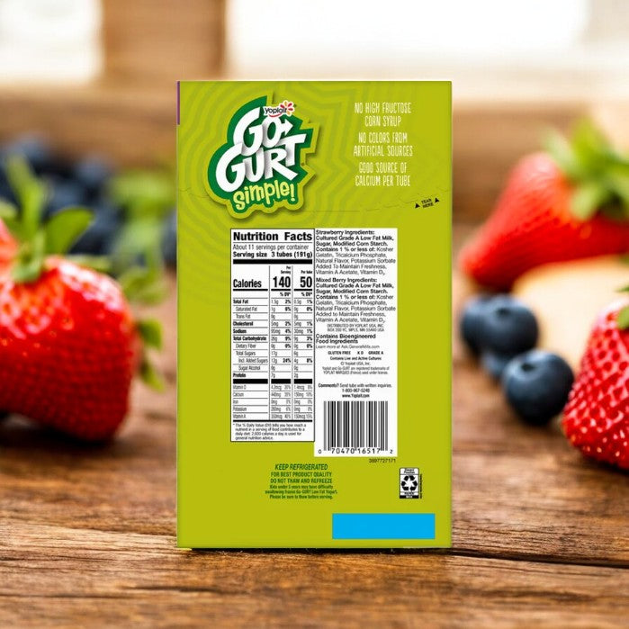 Placed on a wooden table and surrounded by strawberries and blueberries, a box of Yoplait Go-Gurt Simple Low Fat Yogurt Variety (32 Count, 2.25 oz each) displays its nutritional information and product claims such as "No high fructose corn syrup," presenting it as the ideal kids’ snack. Enjoy this convenient and portable yogurt wherever you go!