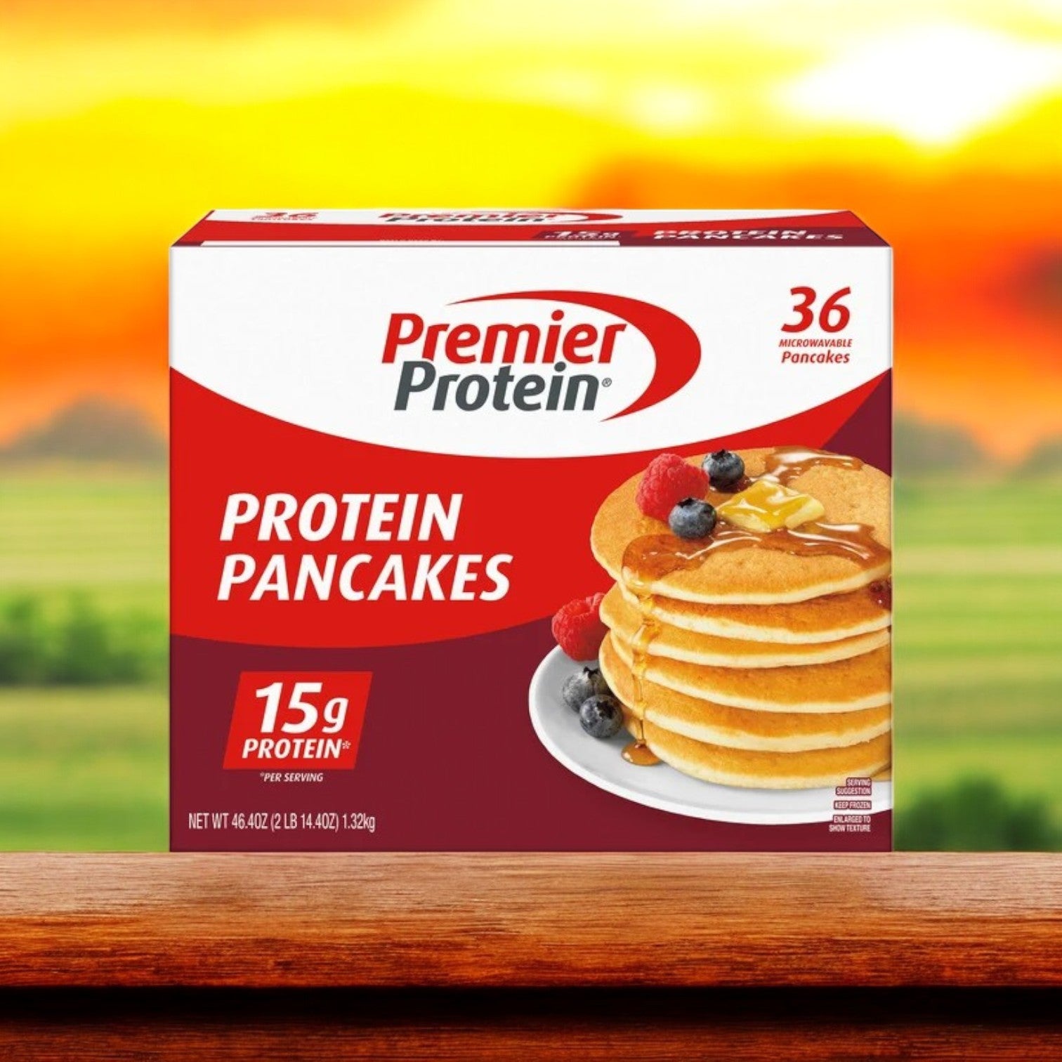 A box of Premier Protein Pancakes – 36-Count -3 Count rests on a wooden surface with a sunrise backdrop, highlighting fluffy pancakes topped with berries and syrup. Enjoy 15g of protein per serving in this low-sugar delight by Premier Protein for a guilt-free breakfast treat.