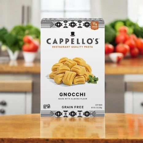 A box of Cappello's Gnocchi Pasta- 3 Count, made with almond flour, rests on a kitchen counter. In the background, fresh vegetables are blurred, highlighting a flawless fusion of paleo-friendly pasta treats.