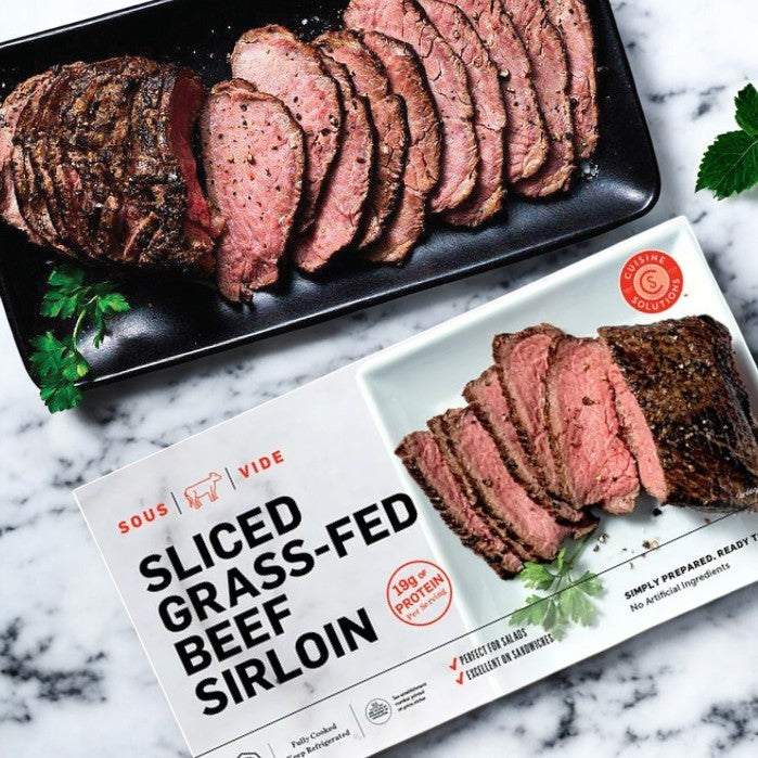 Easy Lunches' Cuisine Solutions Sliced Grass-Fed Beef Sirloin, 1-count, is elegantly presented beside a plate of perfectly sliced beef on a marble surface, accented with garnishes—perfect for those who savor quality and flavor in every protein-packed bite.