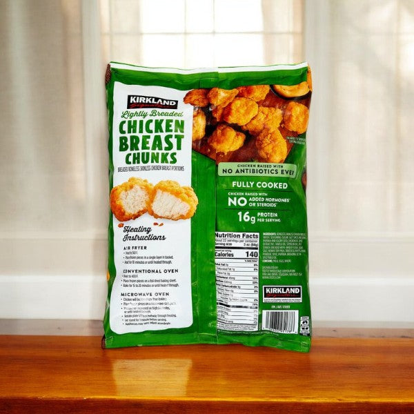 A package of Kirkland Signature Lightly Breaded Chicken Breast Chunks, weighing a total of 12 pounds across three bags, rests on a wooden surface, showcasing nutrition facts and cooking instructions. These pieces provide versatile cooking options, making them an ideal choice for any meal.