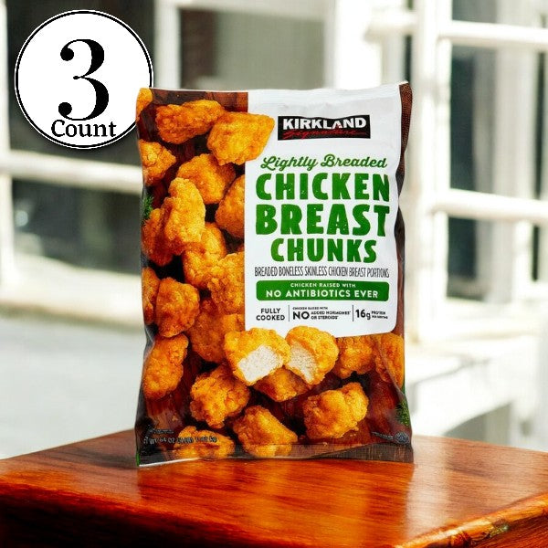 A package of Kirkland Signature Lightly Breaded Chicken Breast Chunks sits on a wooden surface, prominently featuring a circular label that reads "3 Bags." The packaging emphasizes "Lightly Breaded" and "No Antibiotics Ever," ensuring versatile cooking options for any meal.